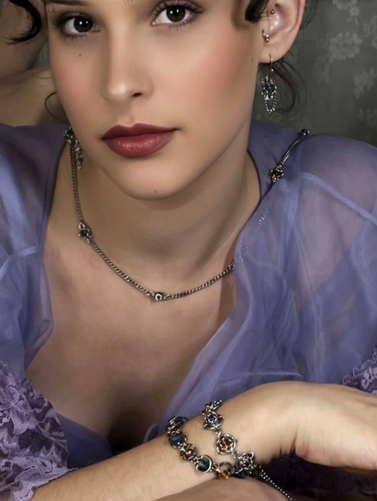 Woman wearing a purple top with jewelry including a necklace, bracelet, and earrings.